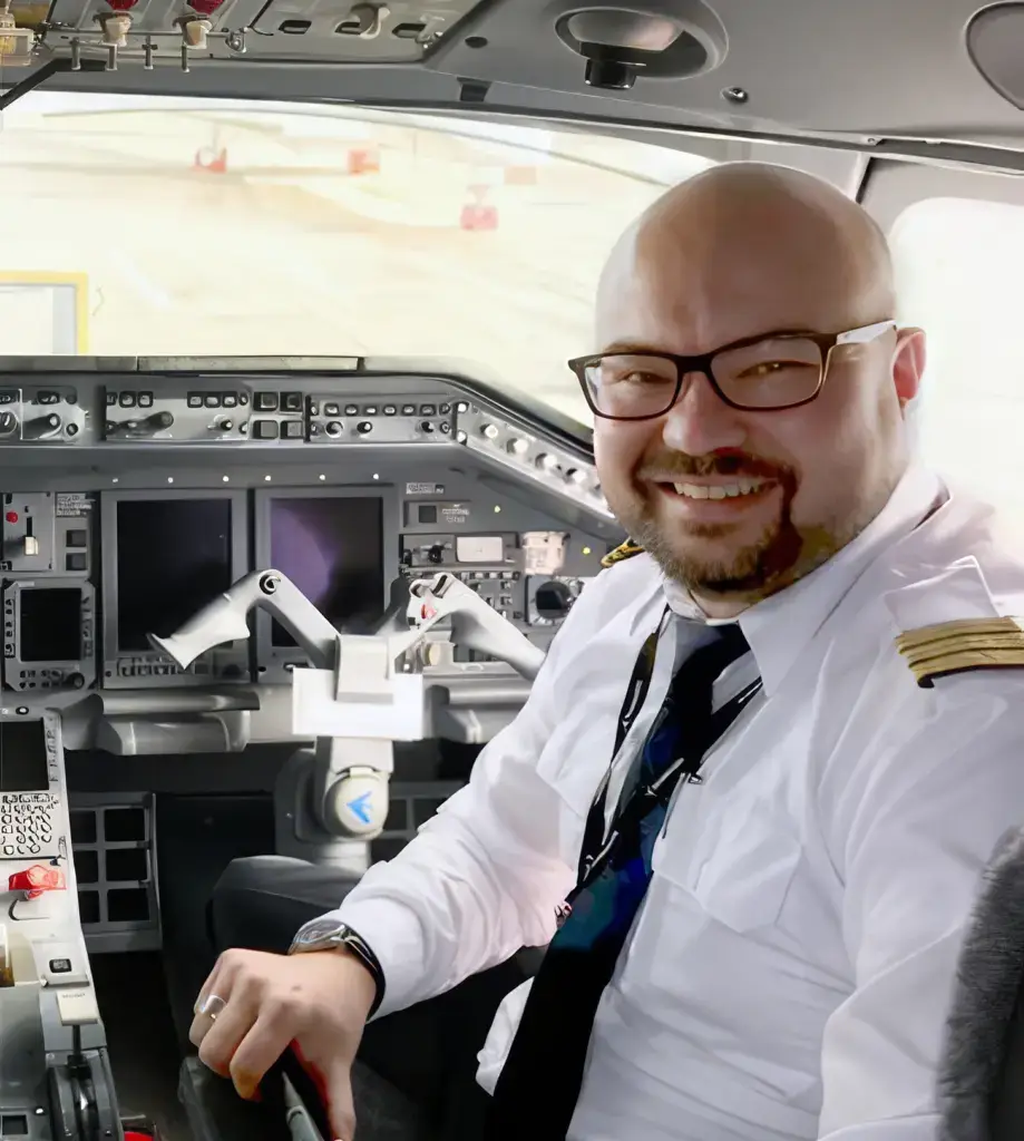 Pilot in Uniform mit Schulterabzeichen sitzt im Cockpit eines Flugzeugs, Hand am Steuerknüppel