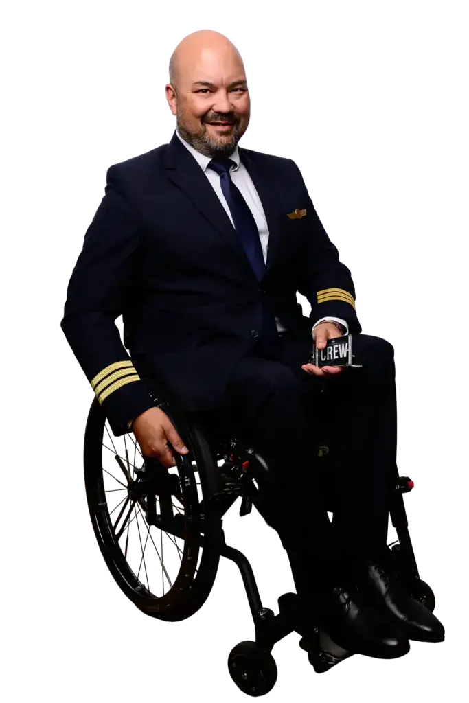 Mann im in Pilotenuniform mit goldenen Streifen an den Ärmeln, sitzt im Rollstuhl und hält einen Crewausweis in der Hand.